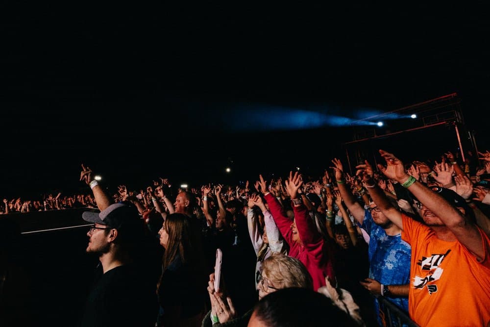 A packed night crowd with hands raised under a blue stage light