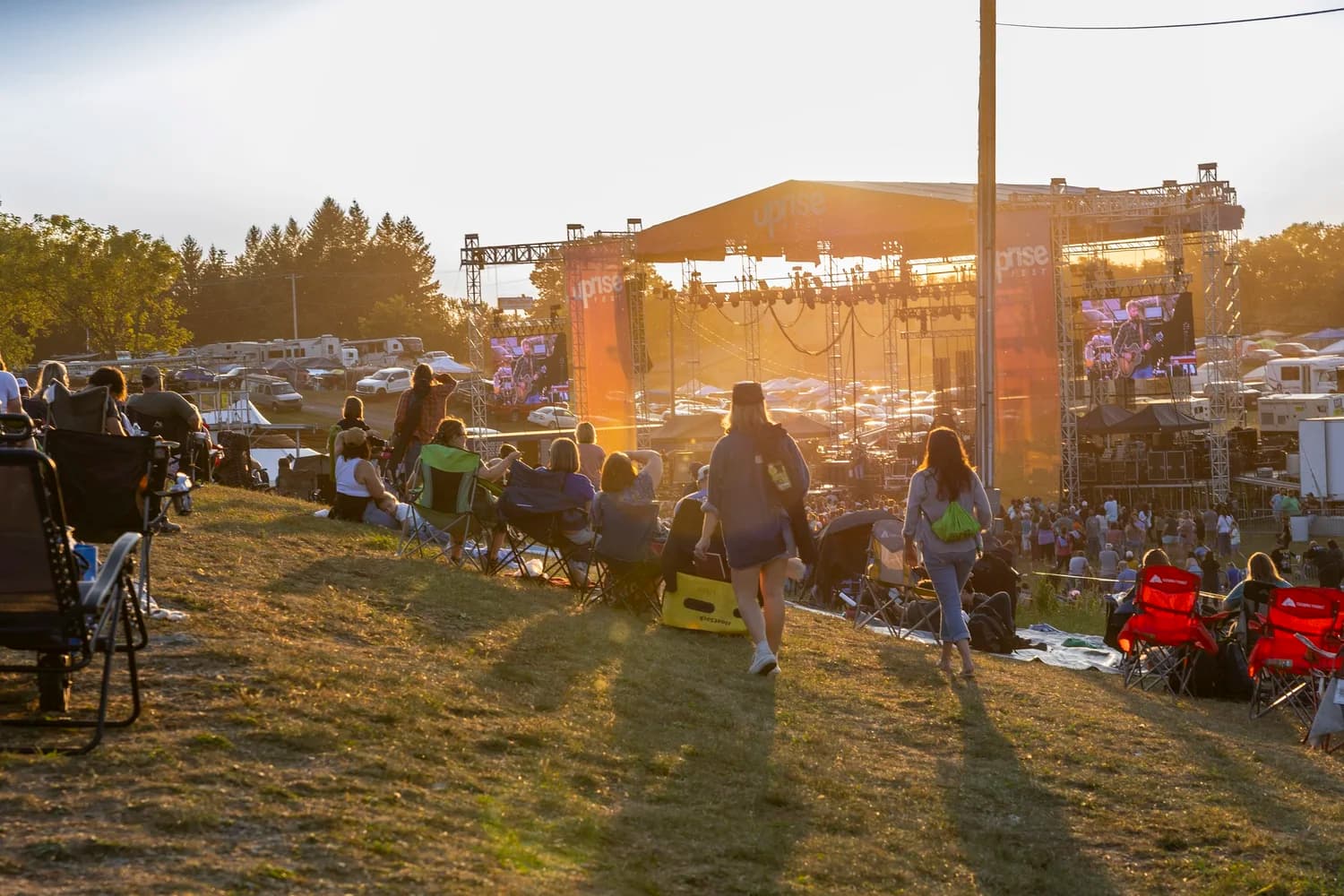 Festival-goers in lawn chairs on the hillside at sunset, the Uprise main stage and its video screens beyond them