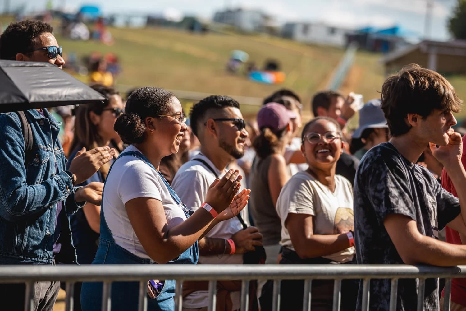 Smiling fans in wristbands clapping along at the front barrier on a sunny afternoon